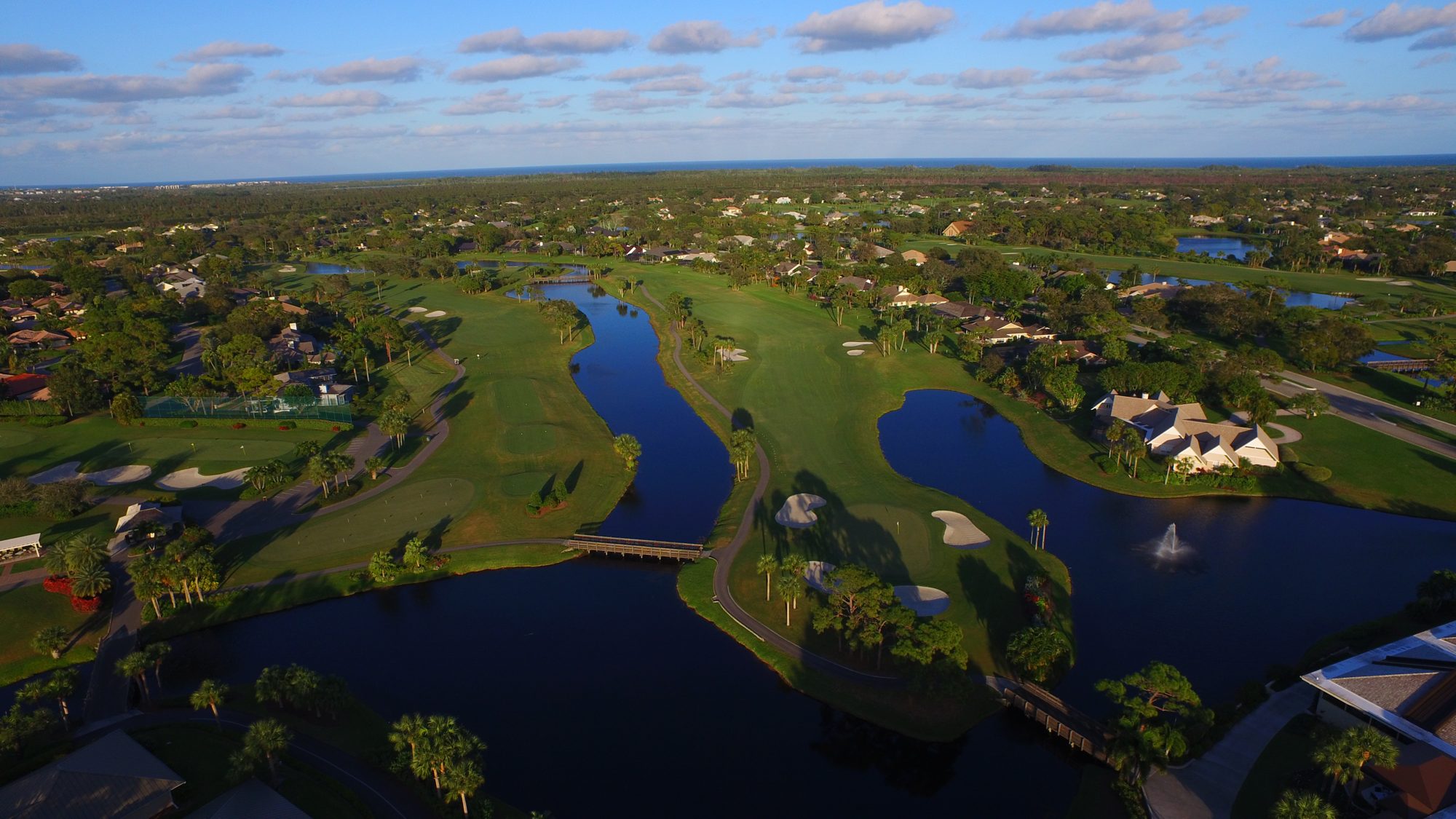 The Mariner Sands clubhouse beside a lake and fountain, with the courses beyond