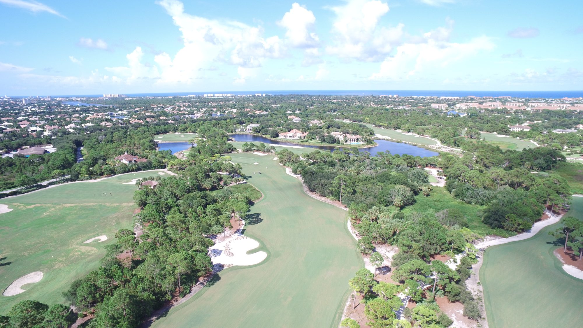 Aerial view of a Bears Club green ringed by white bunkers beside a lake